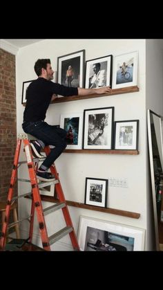 a man on a ladder climbing up the side of a wall with pictures and frames