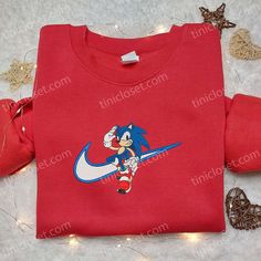 The Sonic x Swoosh Cartoon Embroidered Hoodie is a must-have for any fan of the iconic video game character and Nike’s timeless style. Made with high-quality materials, this hoodie features an eye-catching embroidered design that combines the best of both worlds. With its comfortable fit and trendy look, it’s perfect for everyday wear or as a statement piece. Whether you’re a gamer or a fashion enthusiast, this hoodie is a great addition to your wardrobe. Get ready to turn head Sporty Hoodie With Character Print, Sporty Cotton Sweatshirt With Character Print, Cotton Fandom Sweatshirt For Streetwear, Nike Inspired, Sonic Movie, Sonic X, Best Family Gifts, Nike Gear, Maroon Hoodie