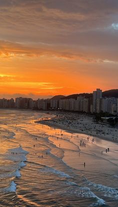 the beach is crowded with people as the sun sets over the city in the distance