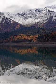 the mountains are covered in snow and fall foliage near a body of water with trees on both sides