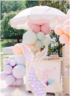 an umbrella and some balloons are on the ground near a table with desserts in it