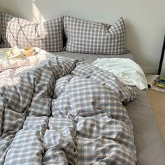 an unmade bed with plaid sheets and pillows