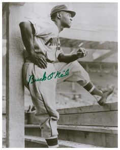 an old black and white photo of a baseball player leaning up against a wall with his foot on the ground