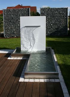 a water fountain in the middle of a wooden decked area next to a building