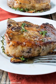 two white plates topped with meat covered in sauce and garnished with green herbs