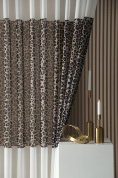 a curtain with leopard print on it next to a white shelf and gold candle holder