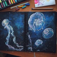 an art journal with jellyfishs and space in the background, surrounded by colored crayons