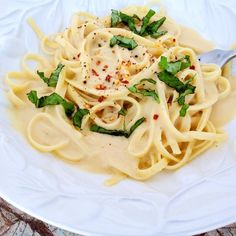 a white plate topped with pasta covered in sauce and garnished with green leaves