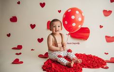 a baby is sitting on the floor with red hearts around him and holding a balloon