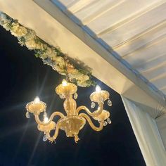 a chandelier hanging from the ceiling under a white canopy with flowers on it