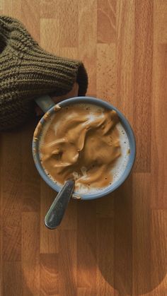 a cup of hot chocolate on a wooden table next to a mitt and sweater