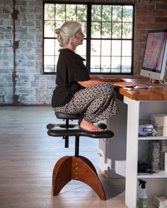 an older woman sitting at a desk with a computer on top of it and looking out the window