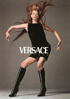 a woman in black dress and knee high boots posing for versa magazine, with her hair blowing in the wind