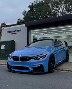 a blue bmw car parked in front of a building with people standing outside the door