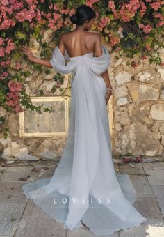 a woman in a white dress standing next to a stone wall with flowers on it