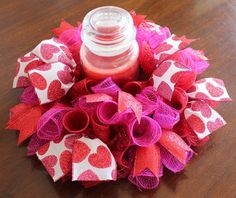 a red and pink heart wreath with a candle in it sitting on a table next to a bottle