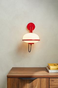 a red and white wall light sitting on top of a wooden cabinet next to a book