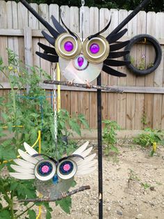 an owl made out of tin cans hanging from a metal pole in front of a fence