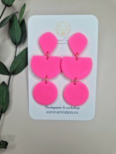 the neon pink statement earrings are on display next to a green plant with leaves in it