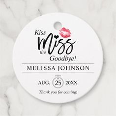 a white round wedding gift tag with the words kiss me, goodbye and a red lipstick on it