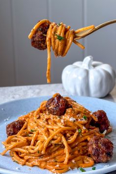 spaghetti with meatballs is being lifted by a fork from a blue plate on a table