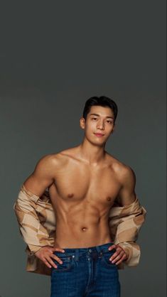 a man with no shirt standing in front of a gray background wearing jeans and holding his hands on his hips