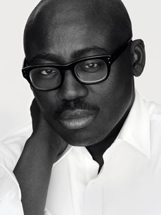 a man with glasses and a white shirt is looking at the camera while leaning on his hand