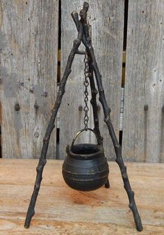 an old fashioned metal pot with chains hanging from it's sides on top of a wooden table