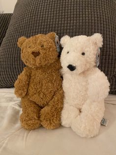 two teddy bears sitting next to each other on a bed in front of a pillow