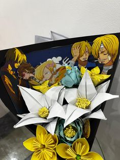 an arrangement of paper flowers with anime characters on them in a black and white box