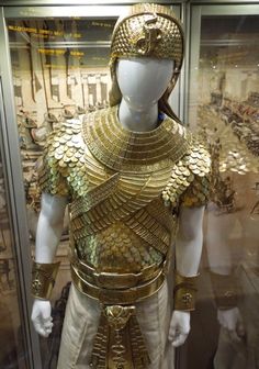 a gold and white costume on display in a glass case with other items behind it