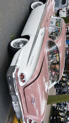 an old pink and white car parked next to other cars