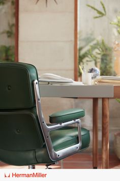 A tight-cropped image of the side of an Eames Executive Chair upholstered in green leather, close to a desk with various accessories on it. Luxurious Chair, California Modern, Charles And Ray Eames, Work Chair