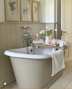 a white bath tub sitting in a bathroom next to two framed pictures on the wall