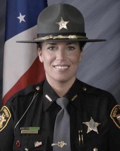 a female police officer in uniform standing next to an american flag and smiling at the camera