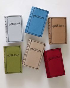 four different colored notebooks sitting next to each other on top of a white surface