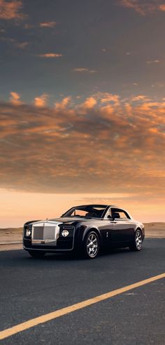 a black rolls royce parked on the side of the road at sunset with clouds in the background