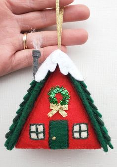 a hand holding a christmas ornament in the shape of a house