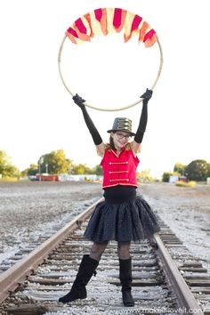 a woman in a red shirt and black skirt is holding a hula hoop over her head