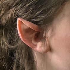 a close up of a woman's ear with hair blowing in the wind and wearing a pair of earrings