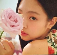 a young woman holding a pink rose in her right hand and looking at the camera