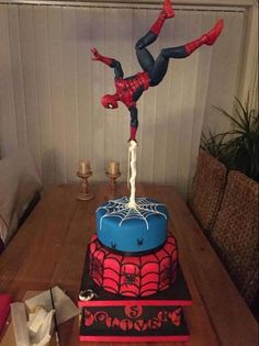 a spiderman cake on top of a table with candles in the background and an image of someone falling off it