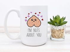 a coffee mug that says i'm nuts about you next to a potted plant