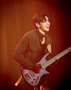 a man holding a guitar in his right hand and smiling at the camera while standing on stage