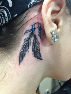 a woman with a tattoo on her ear has a feather and beads behind her ear