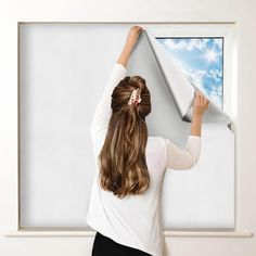 a woman is holding up a paper airplane in front of a white wall with clouds on it