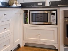 a kitchen with white cabinets and black counter tops, including a microwave built into the wall