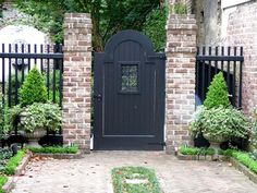 an entrance to a brick house with black gates and potted plants on either side