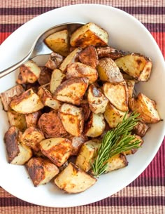 a white bowl filled with potatoes on top of a checkered table cloth next to a spoon