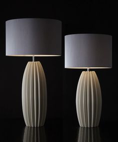 two white lamps sitting next to each other on a black surface with one lamp turned off